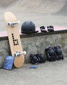 Skateboard, helmet, and protective gear on a concrete ledge with a skate ramp in the background.
